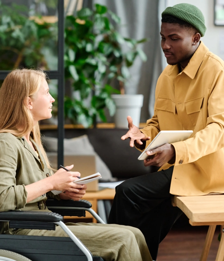 two persons discussing work related topics. one sitting on a table, the other sitting in a wheelchair